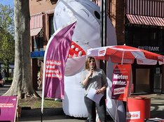 Landessprecherin Sahra Mirow spricht auf der Kundgebung Mieten runter. Im Hintergrund ist ein aufblasbarer Hai und ein Infostand mit dem Schild "Mieten runter" zu sehen.